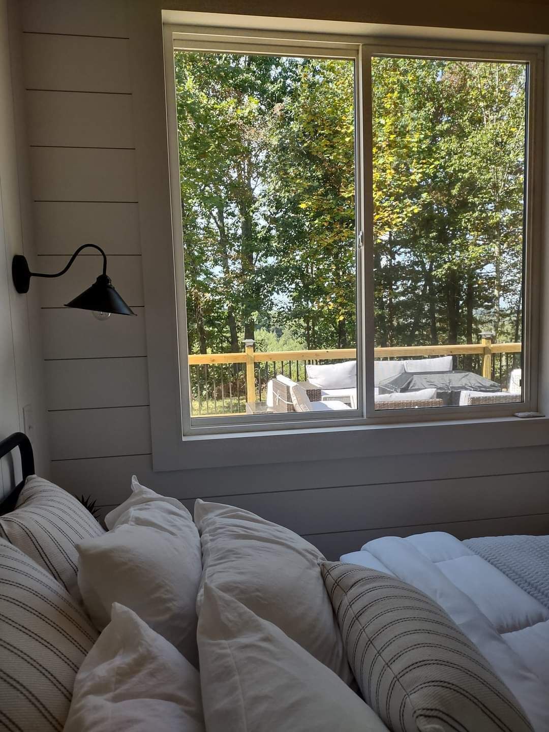 A bedroom with a large window, a bed, and a wall-mounted lamp.