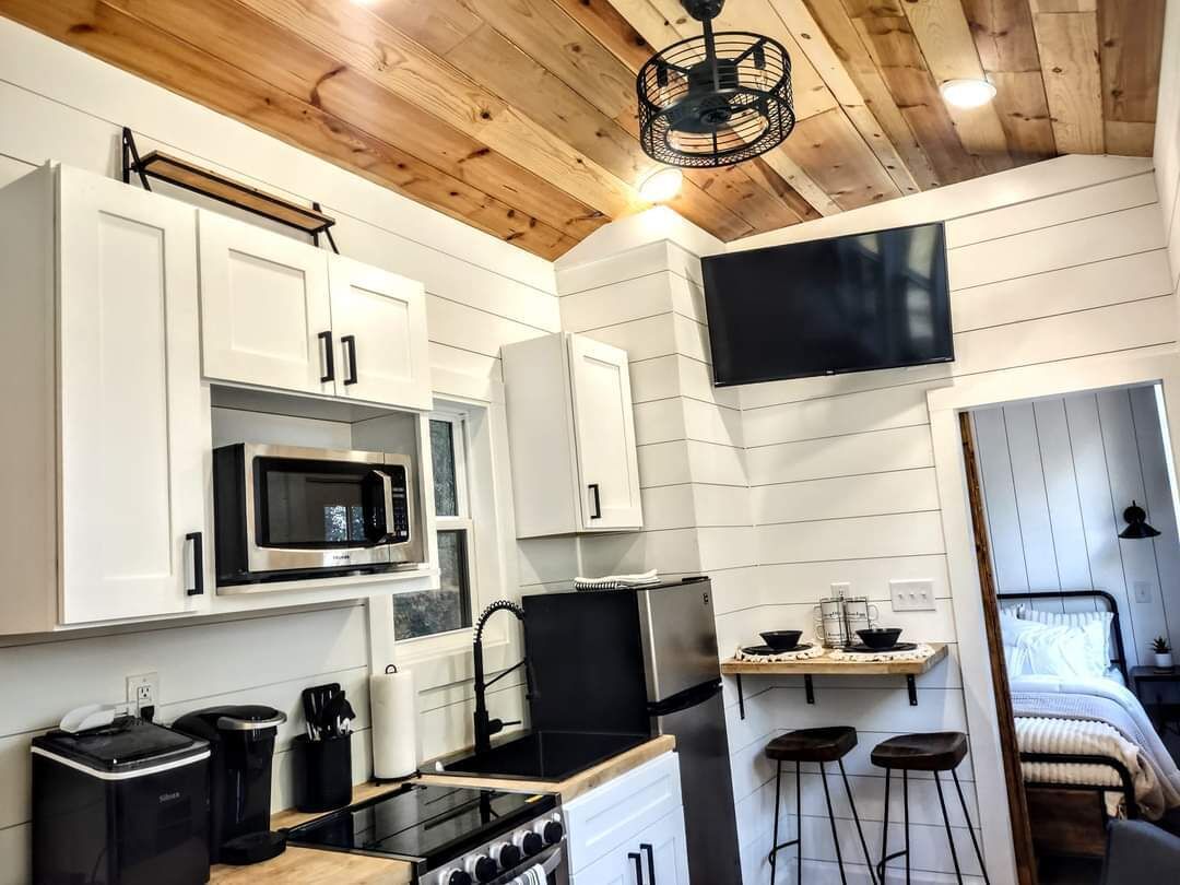 A compact kitchen with white cabinetry, a microwave, a stove, and a small dining area with stools.