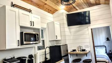 A compact kitchen with white cabinetry, a microwave, a stove, and a small dining area with stools.
