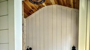 Une chambre avec un plafond en bois, un lit recouvert de linge de lit blanc, deux lampes noires fixées au mur et une petite plante posée sur une table de chevet.