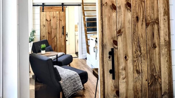 Une pièce dotée d’une porte coulissante de style rustique, d’un canapé en cuir noir et d’un téléviseur fixé au mur.