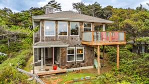 A two-story house with a balcony, surrounded by dense vegetation.