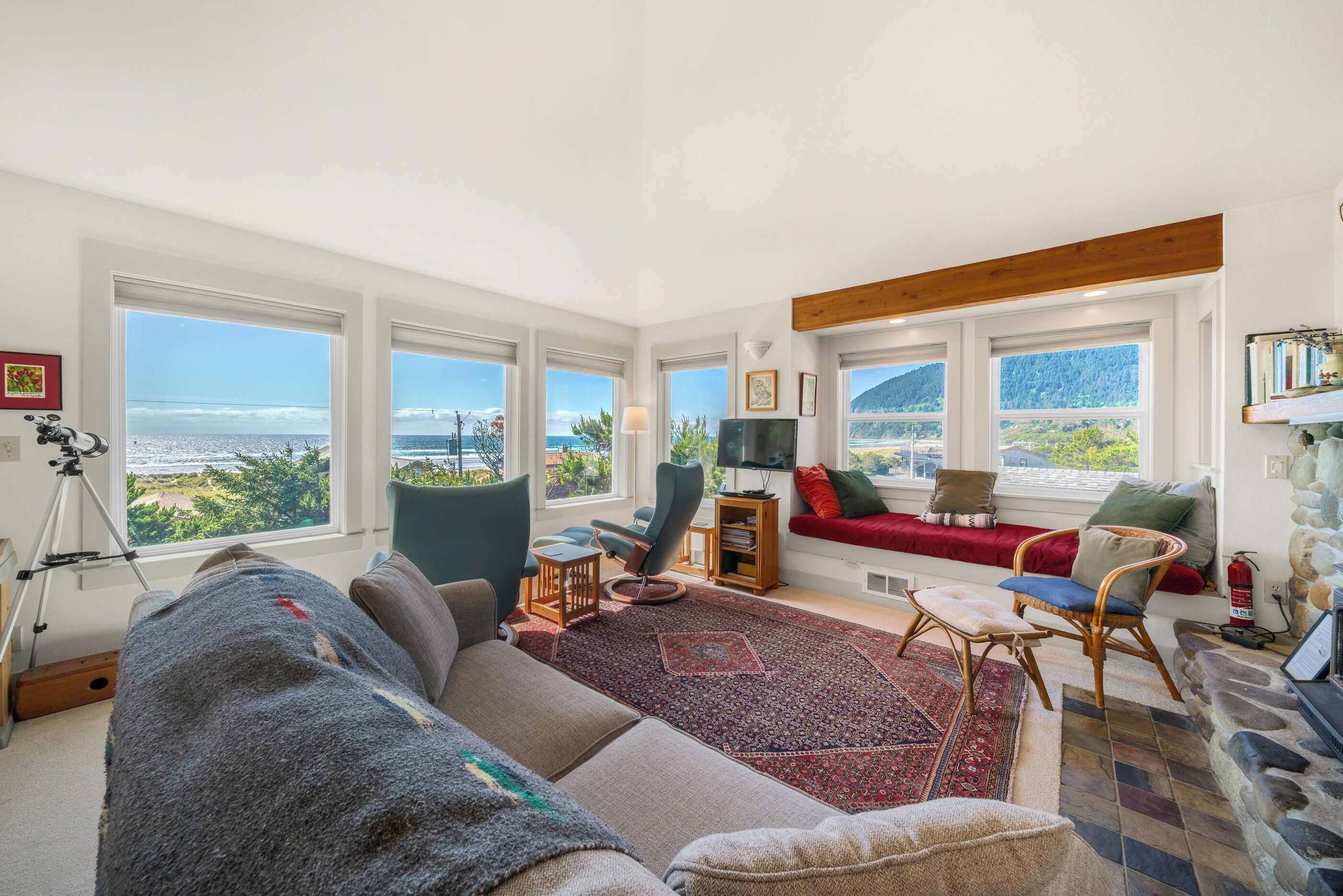 Un salón amplio con ventanas grandes, un sofá rojo, un sillón azul y vista al mar.