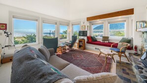 A spacious living room with large windows, a red sofa, a blue armchair, and a view of the sea.