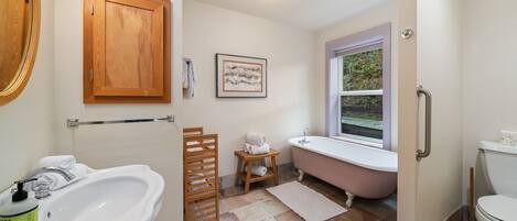 Un baño con lavamanos blanco, mueble de madera, una obra de arte enmarcada, una bañera rosa y un inodoro.