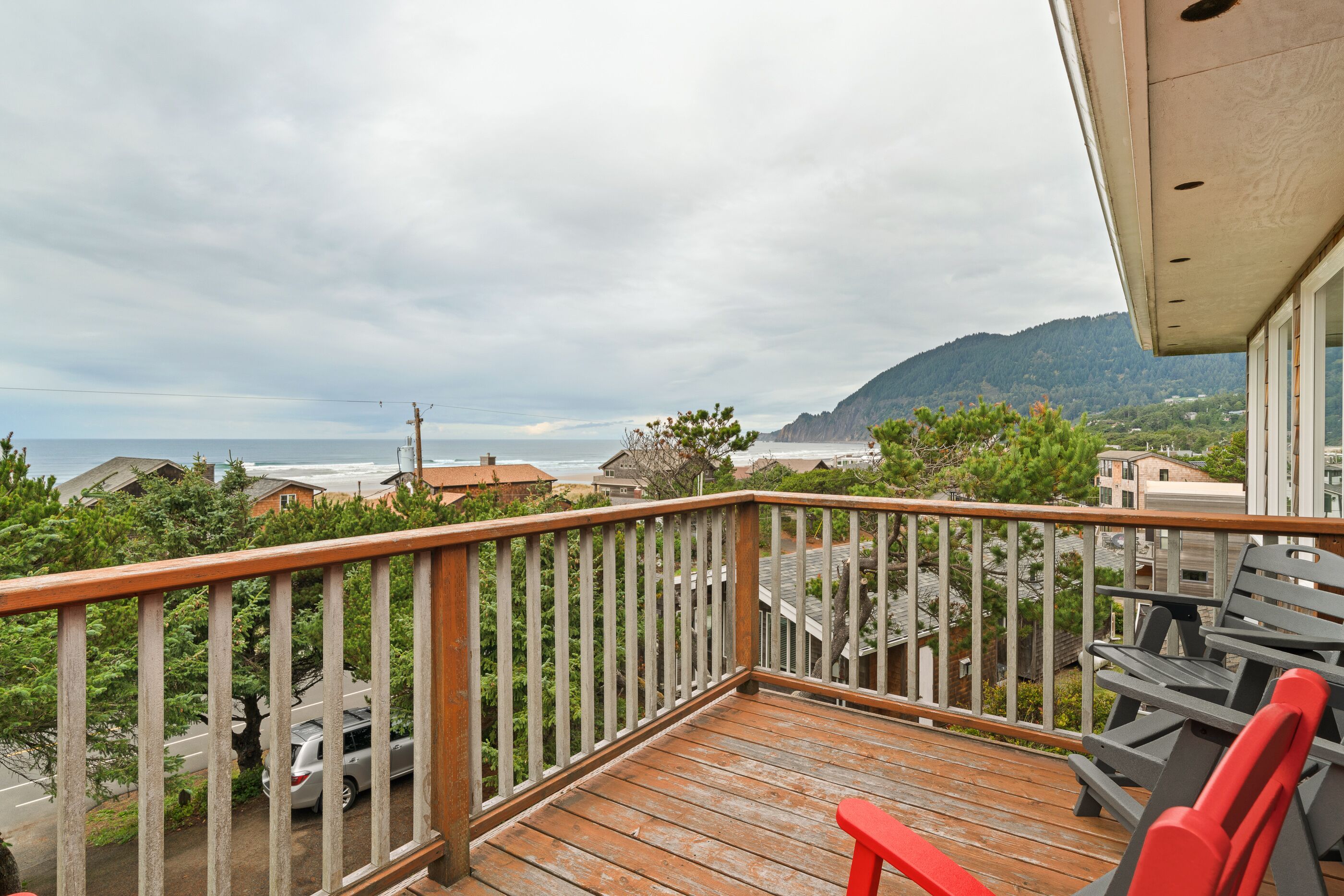 A wooden deck with a railing, overlooking a residential area and a mountain.