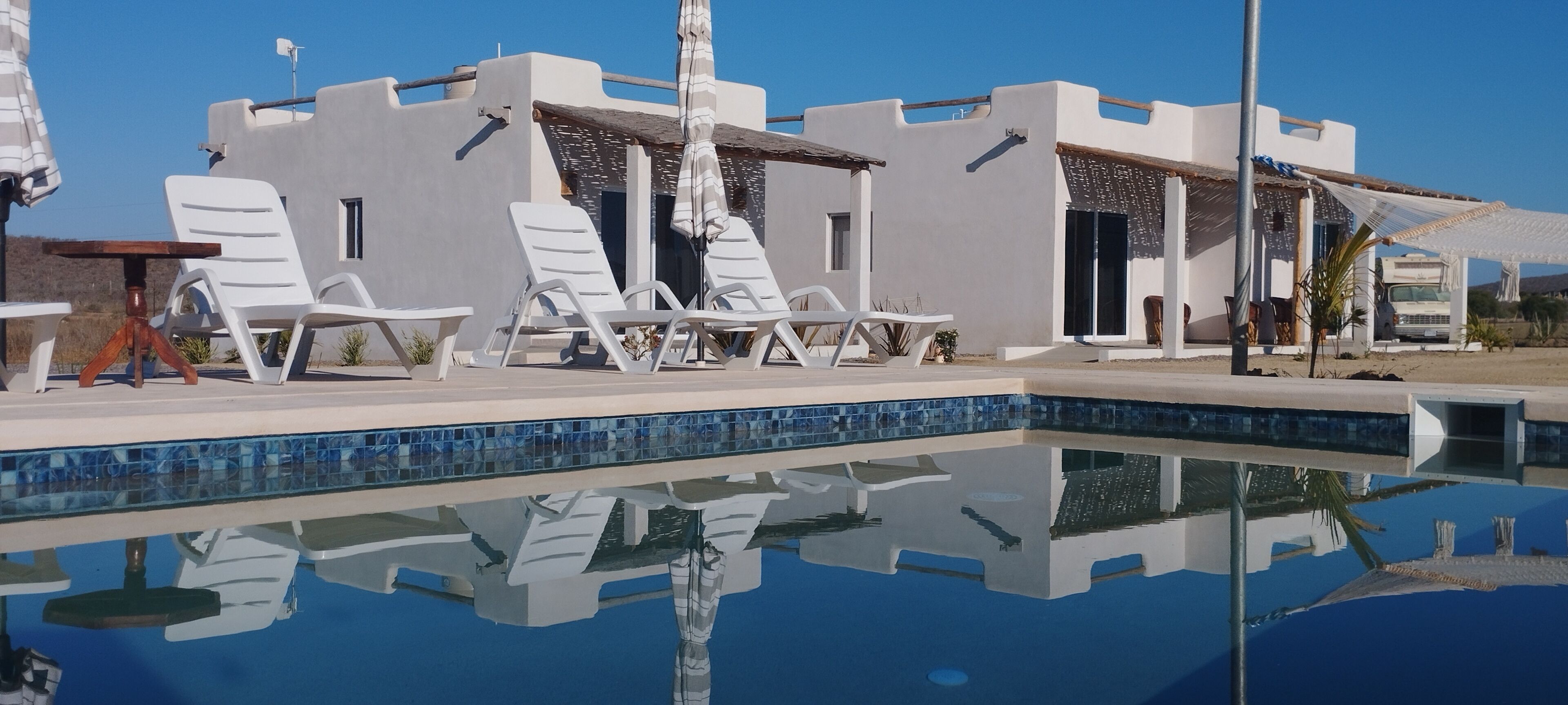 Un espace moderne au bord de la piscine, avec des chaises longues blanches et une piscine dont le fond est recouvert de carreaux de verre.