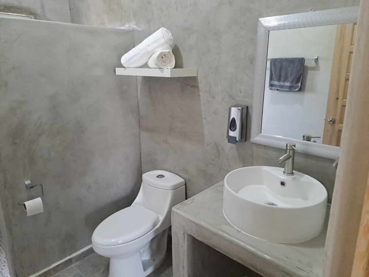 A bathroom with a toilet, a sink, a towel shelf, and a mirror.