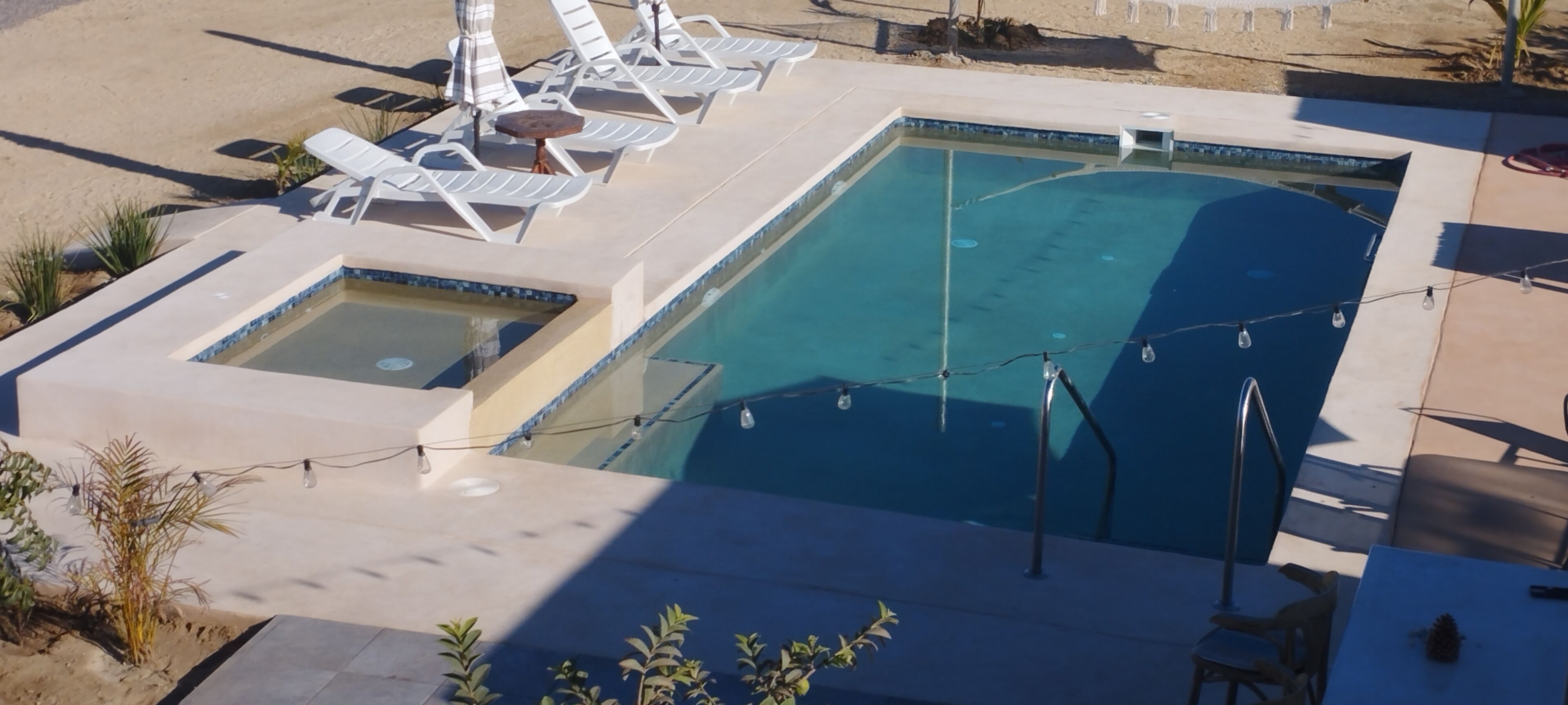 A swimming pool with lounge chairs and a small hot tub area.
