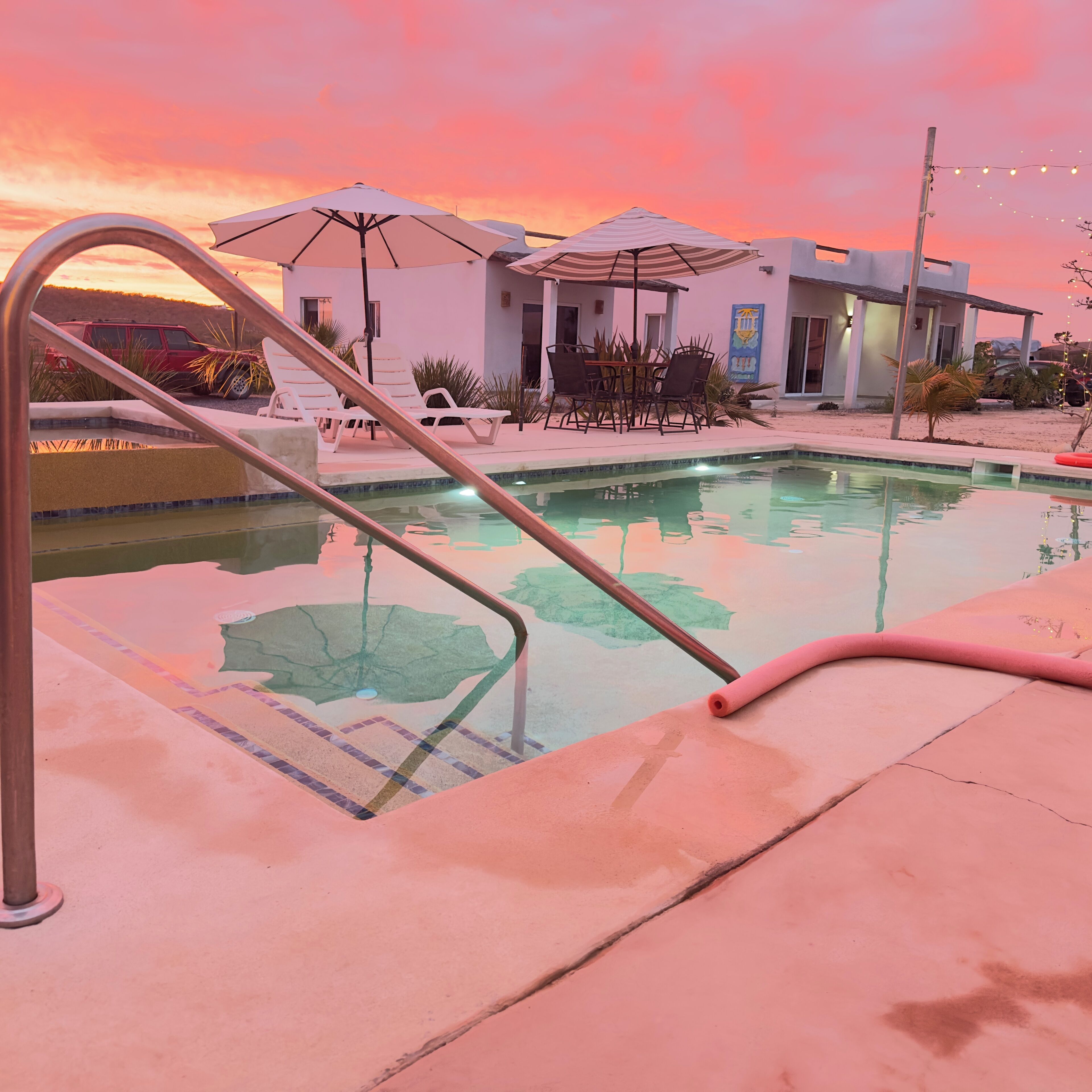 Una piscina con escalera metálica, sillas de descanso y sombrillas.