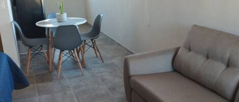 A living room with a beige sofa, a dining table with chairs, and a potted plant.