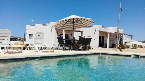 A clear pool with a white building and lounge chairs in the background. - Vista Sierra Laguna (El Pescadero)