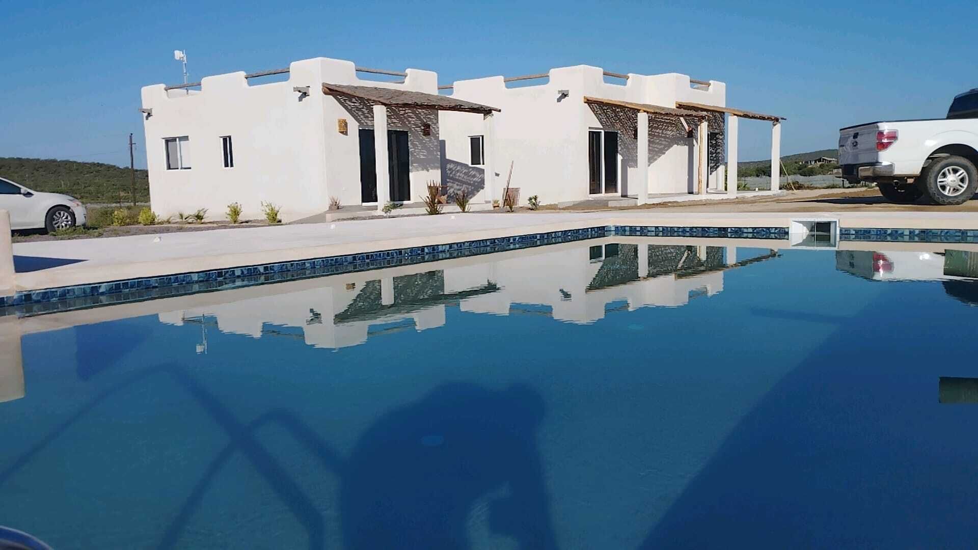 A modern building with a pool, a white car parked nearby, and a clear blue sky.