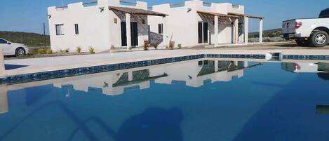 A modern building with a pool, a white car parked nearby, and a clear blue sky.