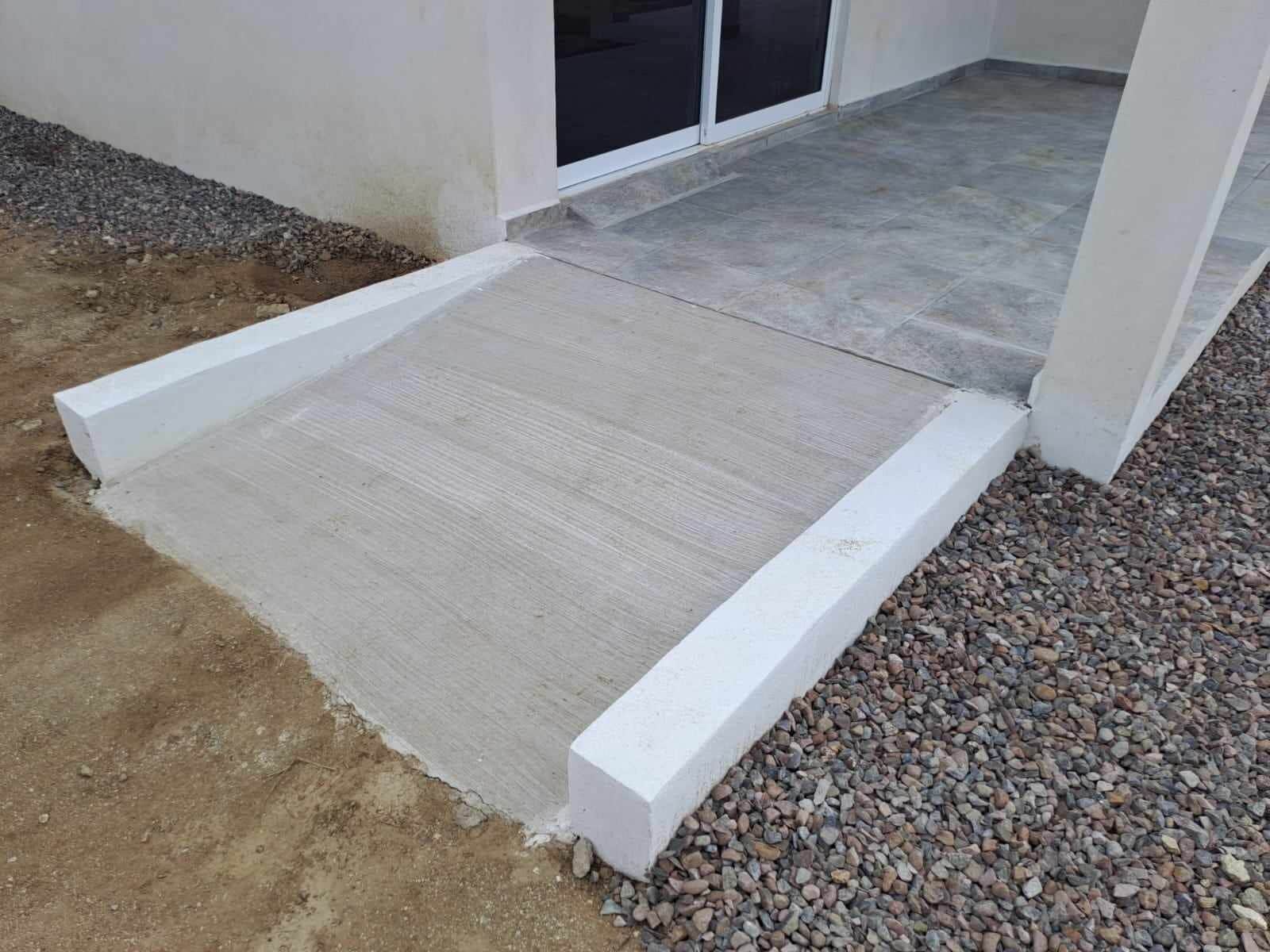 Rampa de concreto que leva à entrada de um edifício, com um caminho de cascalho ao lado.