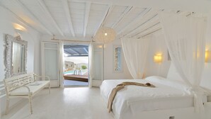 Een slaapkamer in witte tinten met een bed, een bankje en uitzicht op buiten.