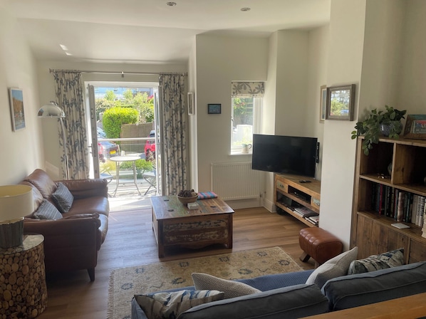 A living room with a sofa, coffee table, TV, bookshelf, and a view to the outside.