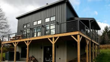 Une maison moderne à deux étages, dotée d’un balcon, de grandes fenêtres et d’une terrasse en bois.