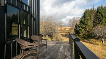 Une terrasse en bois, agrémentée de chaises en osier, qui offre une vue sur une zone boisée et, au loin, sur des arbres et des collines.