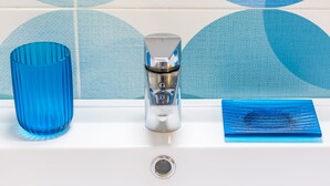 Een wastafel met een blauwe glazen vaas, een metalen kraan en een blauwe glazen schaal.