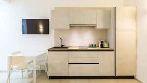 Een moderne keuken met een wit aanrecht, een inbouwoven en een koelkast. Links bevindt zich een eettafel met stoelen.
