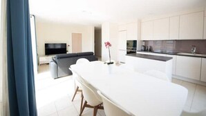 A modern kitchen with white cabinets, a dining area with a white table and chairs, and a living area with a sofa and TV. - Beautiful 3 bedroom apartment 20 min from Paris

 (Vigneux-sur-Seine)