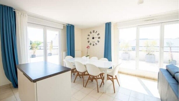 A bright room with a dining table and chairs, a clock on the wall, and large windows. - Beautiful 3 bedroom apartment 20 min from Paris

 (Vigneux-sur-Seine)