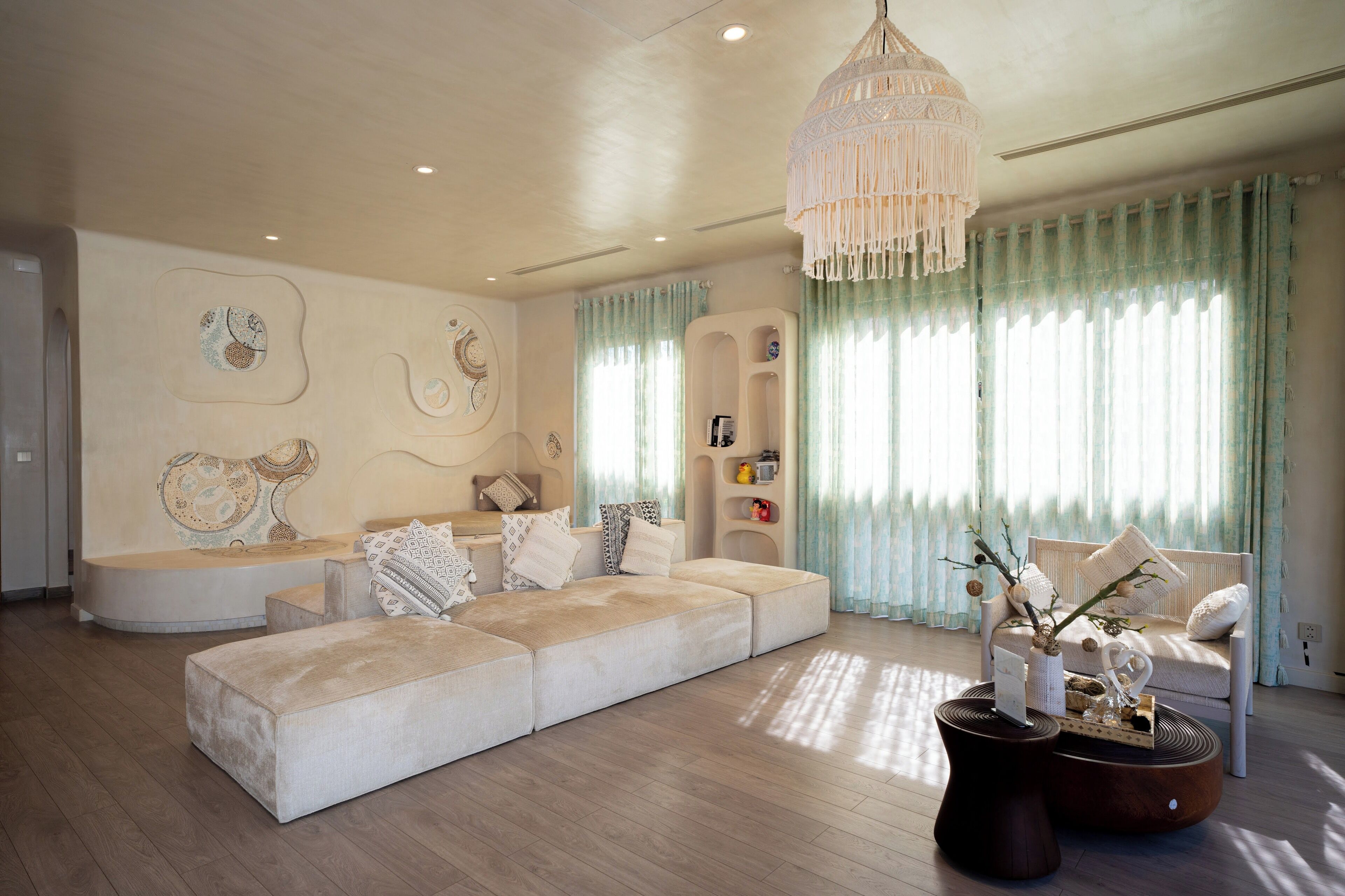 A modern living room with a large sectional sofa, a decorative chandelier, and a built-in shelving unit.