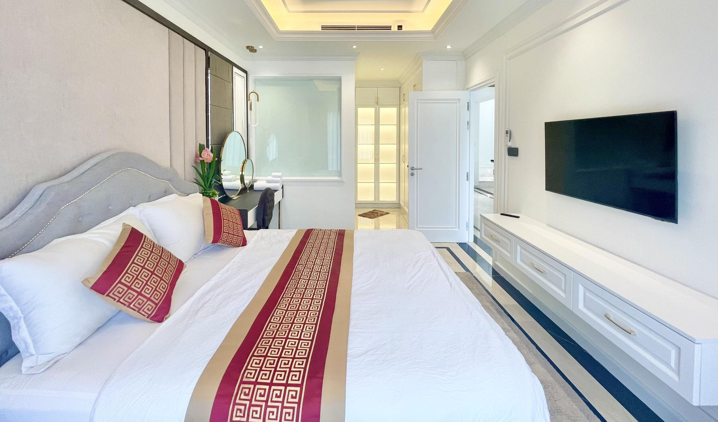 A hotel room with a large bed, a TV, a desk, and a bathroom visible through an open door.