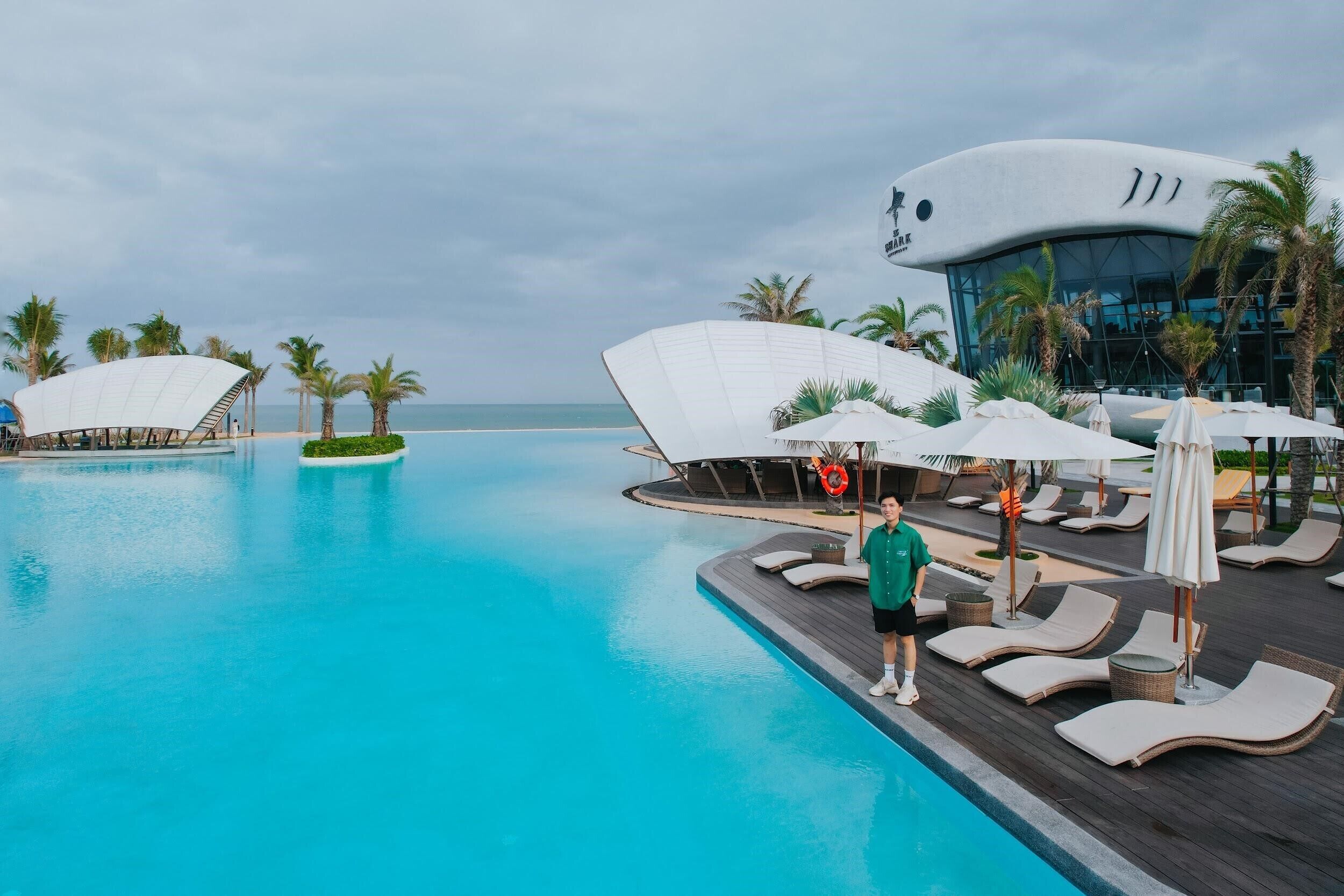 A modern hotel with a large swimming pool, lounge chairs, and umbrellas.