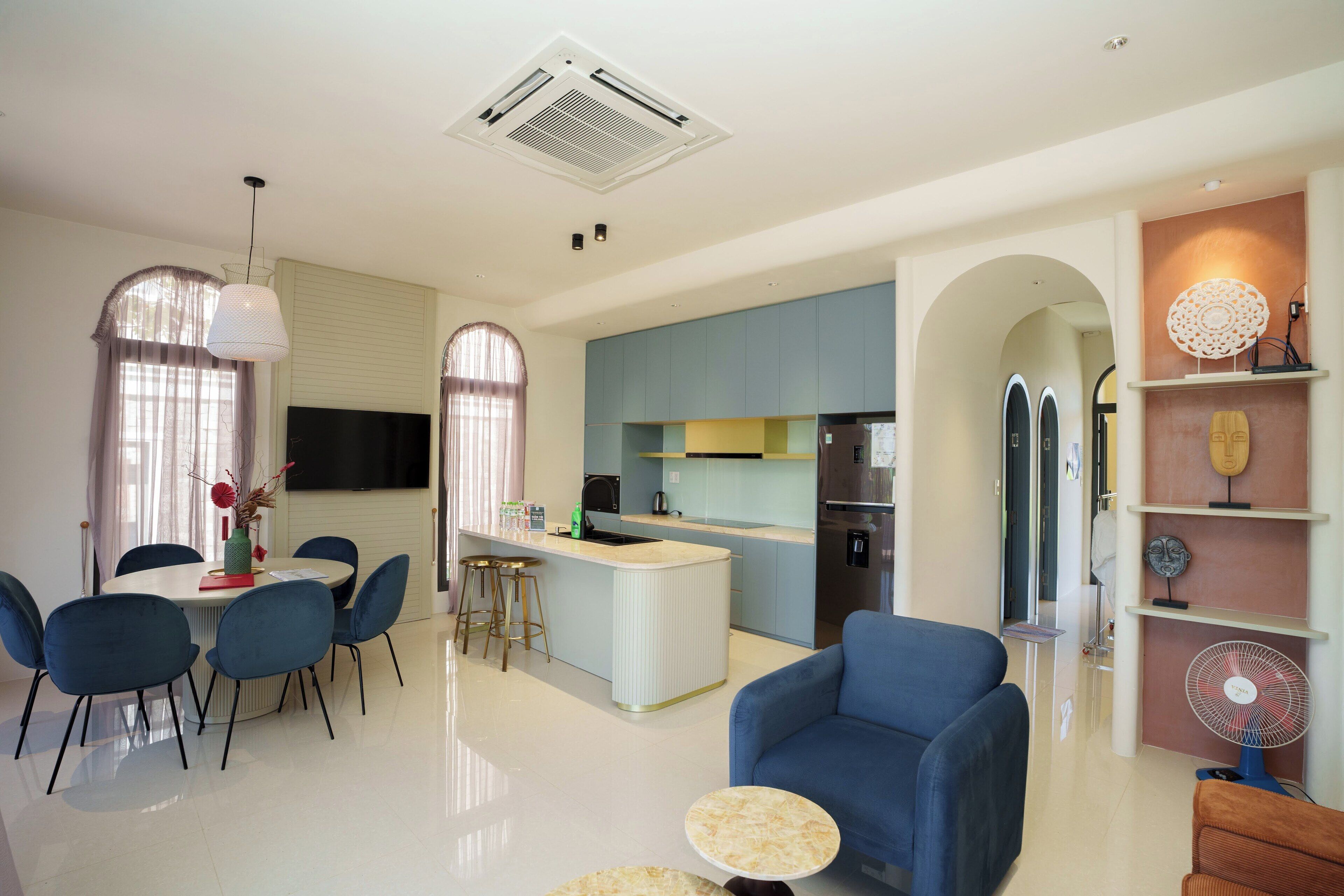 A modern kitchen with a central island, blue chairs, a dining table, and a blue sofa.