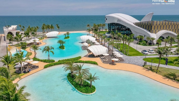 Un complexe hôtelier doté d’une grande piscine, de palmiers et d’un bâtiment moderne au design original.