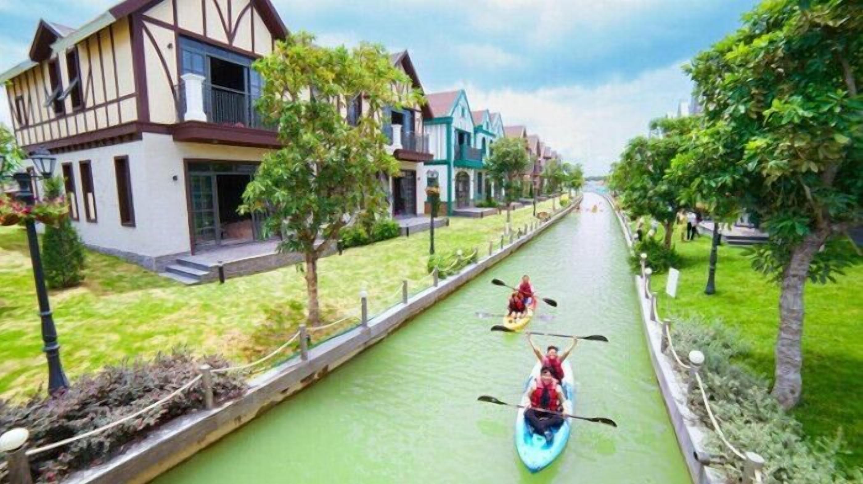 A canal with two kayaks, surrounded by houses and greenery.