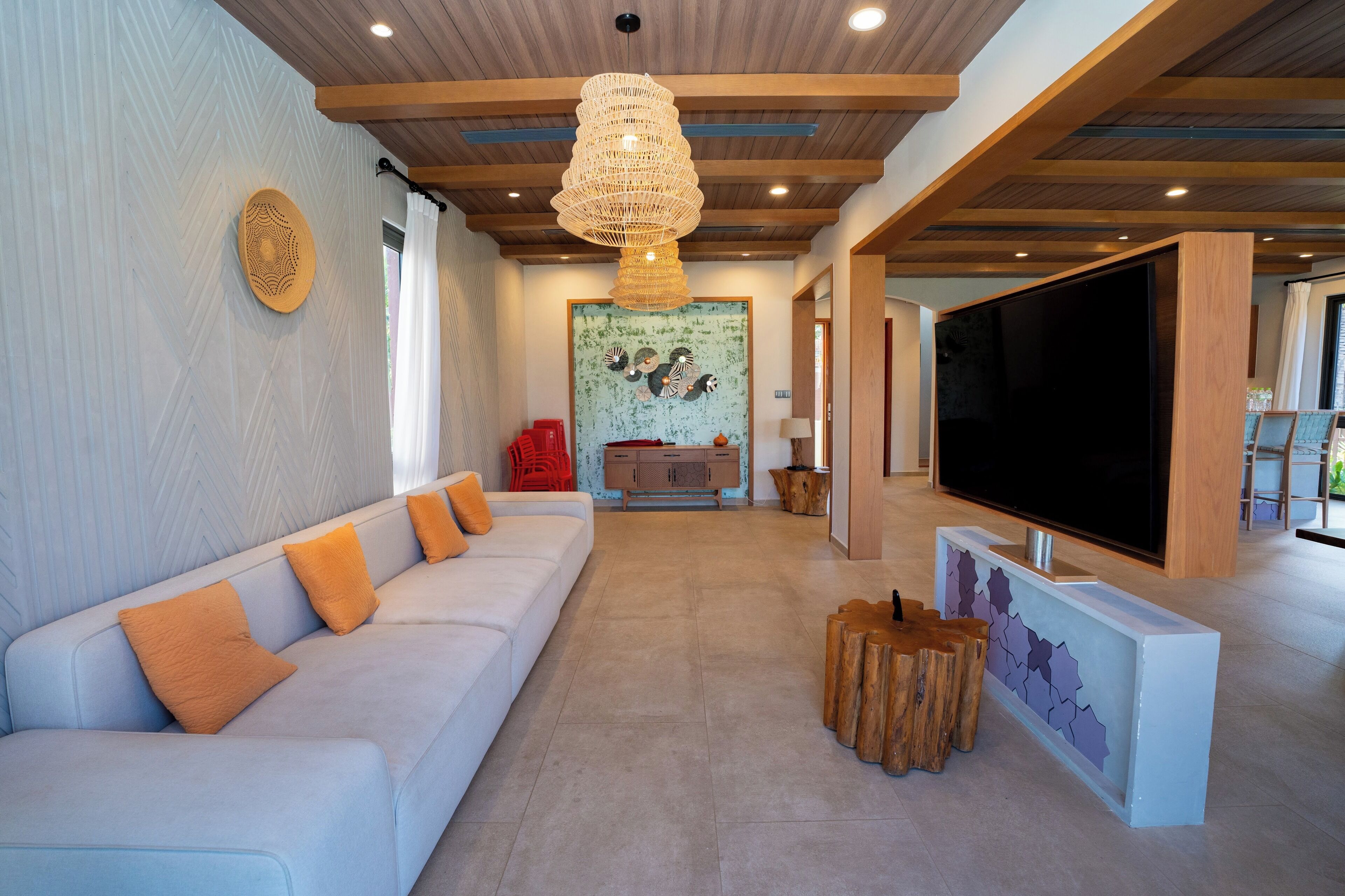 Una sala de estar moderna con un sofá blanco, vigas de madera en el techo, un televisor grande y un elemento decorativo en la pared.