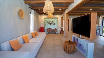 Una sala de estar moderna con un sofá blanco, vigas de madera en el techo, un televisor grande y un elemento decorativo en la pared.
