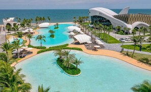 A resort with a large pool, palm trees, and a modern building with a unique design. - Happy Stay (Ho Chi Minh City)