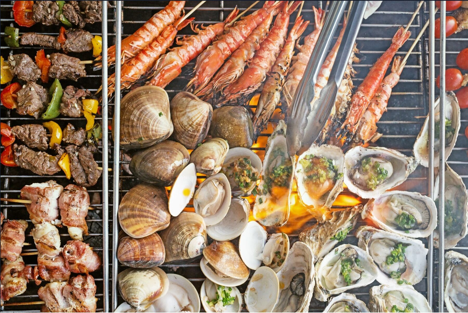 A variety of grilled seafood including shrimp, clams, and oysters on a grill.