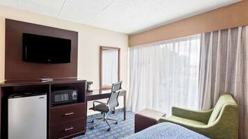 A hotel room with a bed, a desk with a computer, a refrigerator, a microwave, a TV, and a window with curtains.