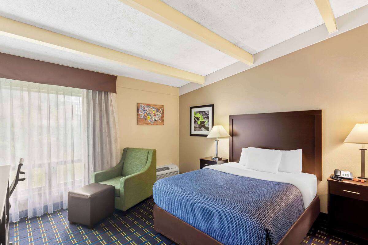 Una habitación de hotel con una cama, una silla, un escritorio y una lámpara.