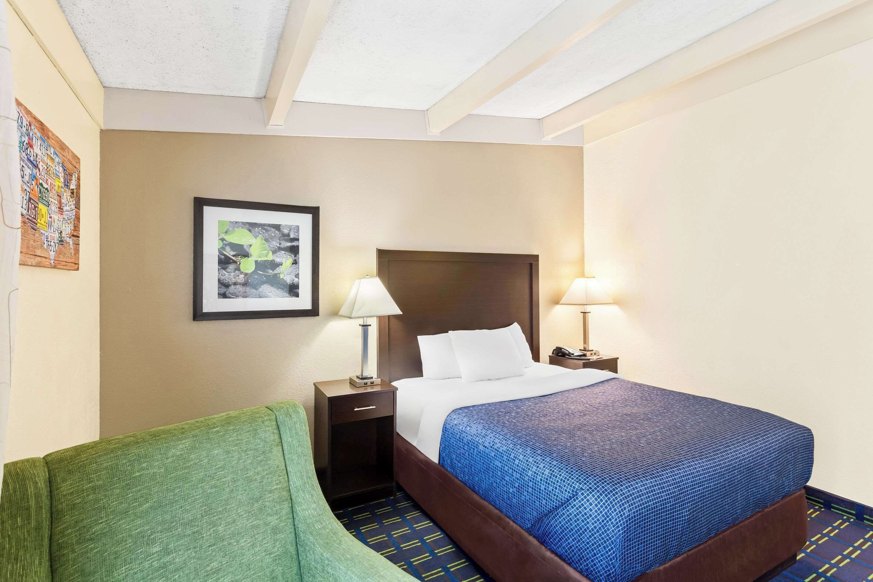 A hotel room with a bed, two bedside tables with lamps, a framed picture on the wall, and a green armchair.