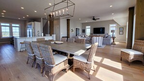 Un'ampia zona giorno con un grande tavolo da pranzo circondato da sedie in vimini, una cucina sullo sfondo e una ventola a soffitto.