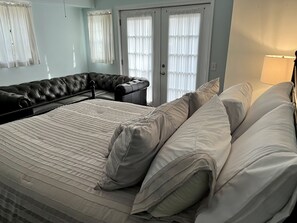 Una cama bien hecha con sábanas blancas y una silla de cuero negro en una habitación con paredes azul claro y cortinas blancas.