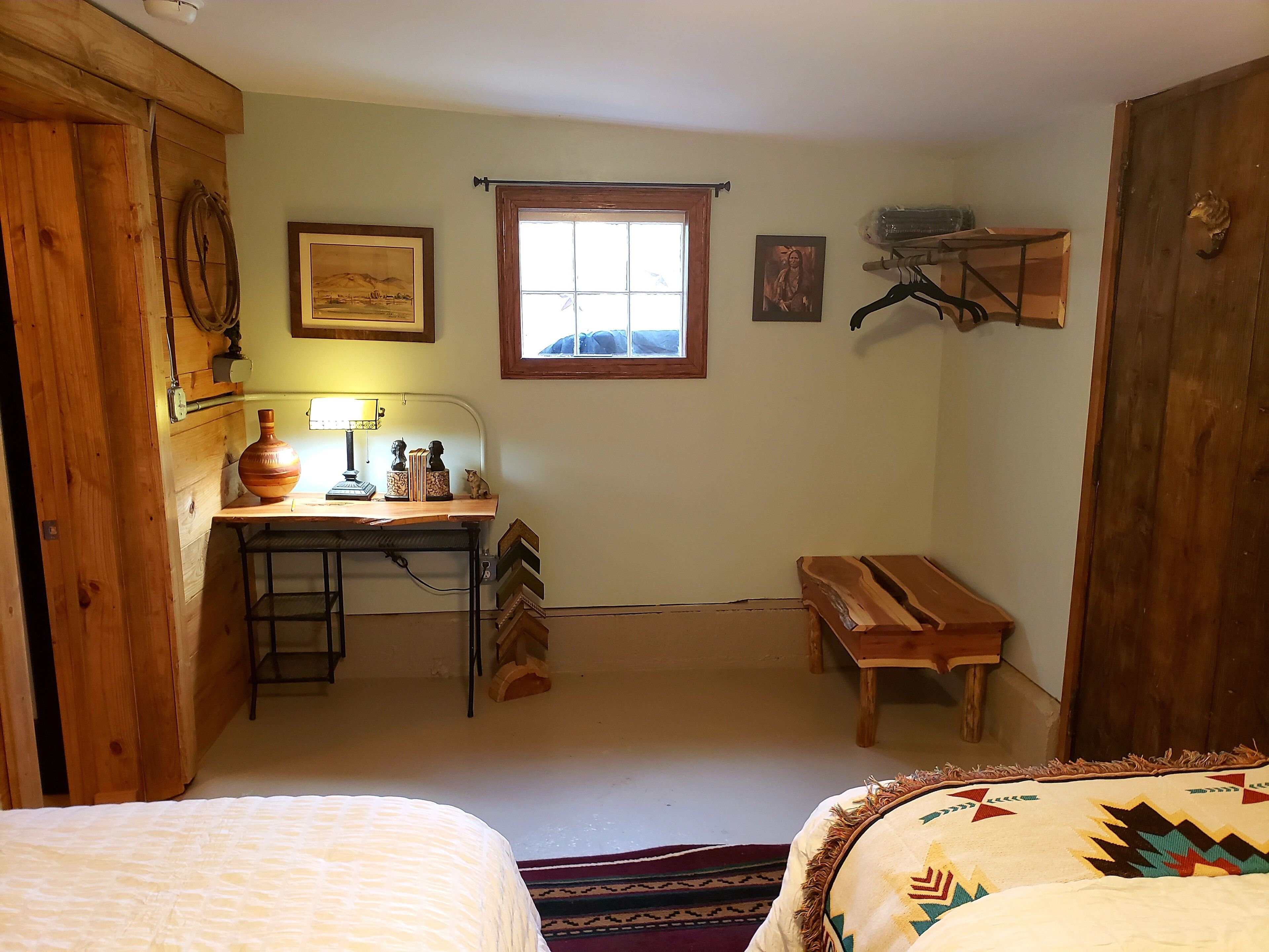 A cozy room with a wooden desk, a window, a bed with a patterned blanket, and a bench.