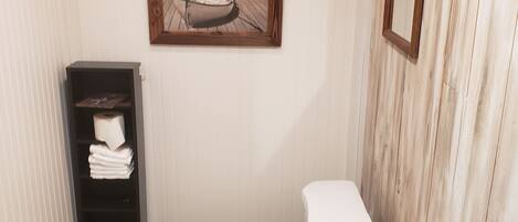 Un baño con inodoro, piso de madera, estante con toallas y un cuadro en la pared.