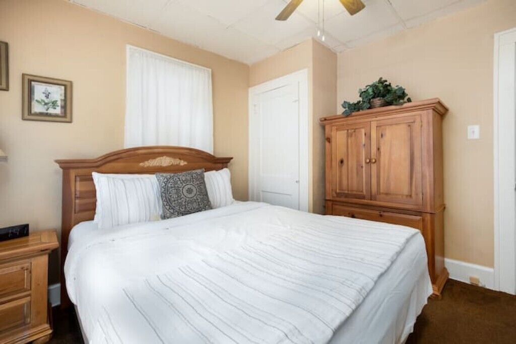 A bedroom with a large bed, wooden headboard, a nightstand, a wardrobe, and a ceiling fan.