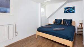 Een slaapkamer met een bed, een raam, een radiator, een schilderij en een nachtkastje.