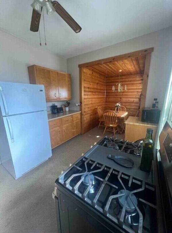 A compact kitchen with a gas stove, wooden cabinets, a refrigerator, and a dining area with chairs.