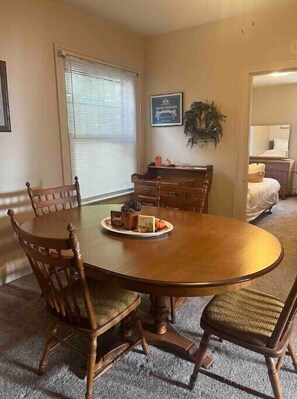 A dining room with a wooden oval table, four chairs, a sideboard, and a window with blinds.