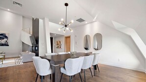 Un espace de salle à manger moderne avec une table centrale, des chaises à revêtement gris et un lustre contemporain.