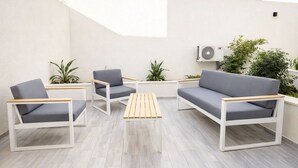 A modern outdoor seating area with a wooden table, grey sofas, and white frames. - Victor Hugo (La Marsa)